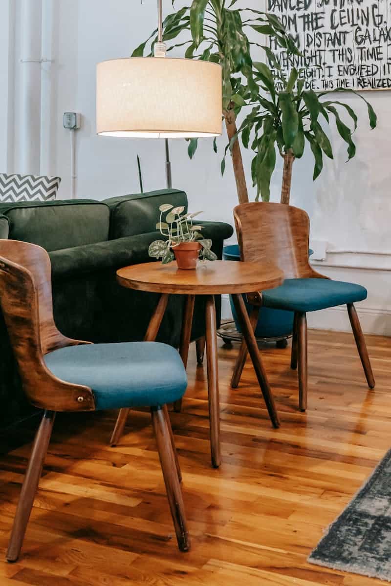 Creative wooden table and chairs placed near potted green palm and floor lamp in cozy light living room of comfortable apartment